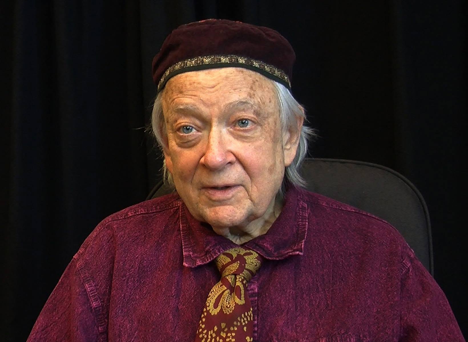 Portrait of Rabbi Hanan Sills, wearing a velvet kippah and a purple shirt with a patterned tie.